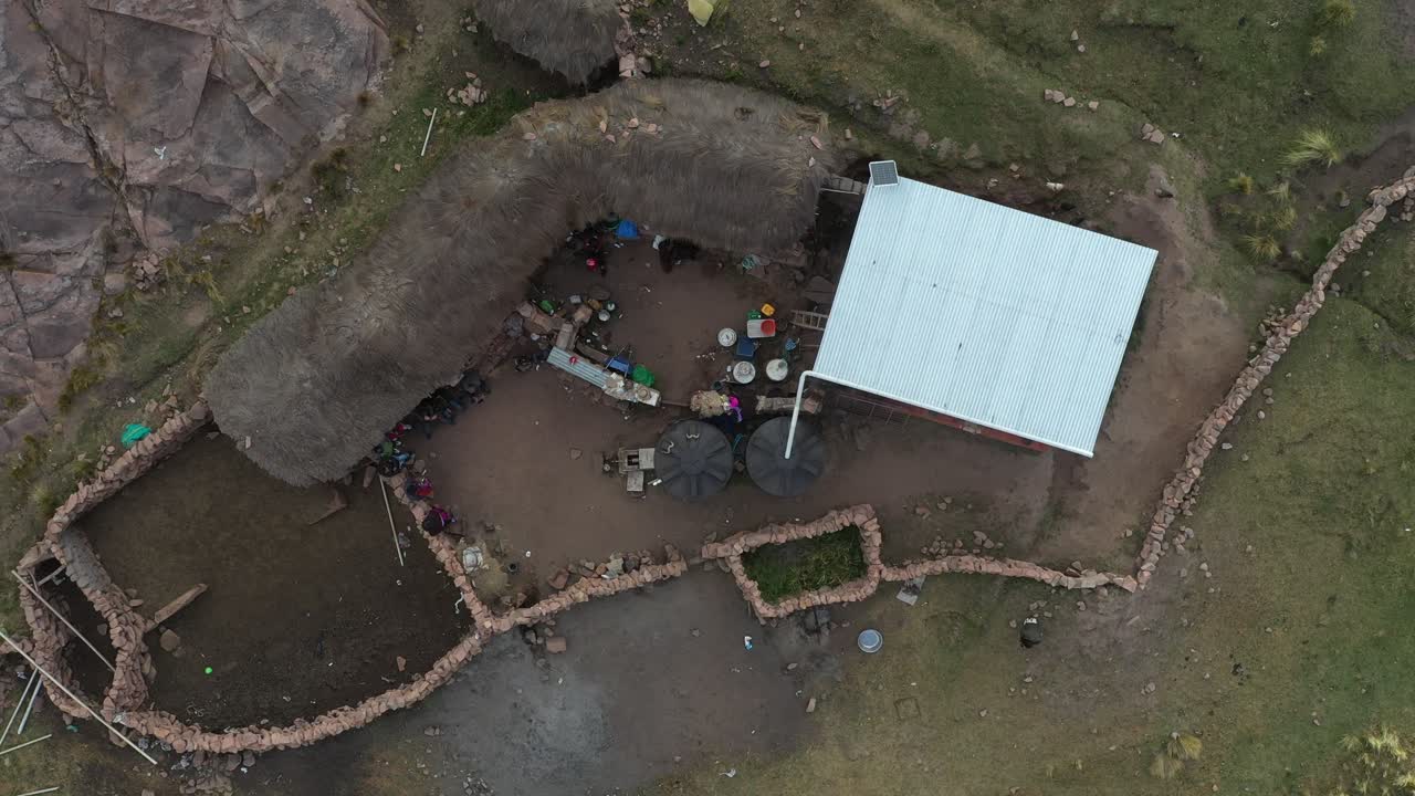 vista aérea de un dron sobre una pequeña casa de campo rodeada de paredes de piedra junto a granjas de terrazas incas en los andes bolivianos durante el día