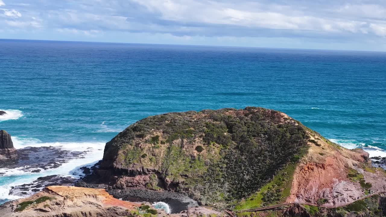 Drone camera smoothly pans over rugged island, blue ocean, and dramatic coastline in bright daylight