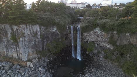 drone aerial view in south korea flying in front of a waterfall over the sea rocky area backwards jeju island