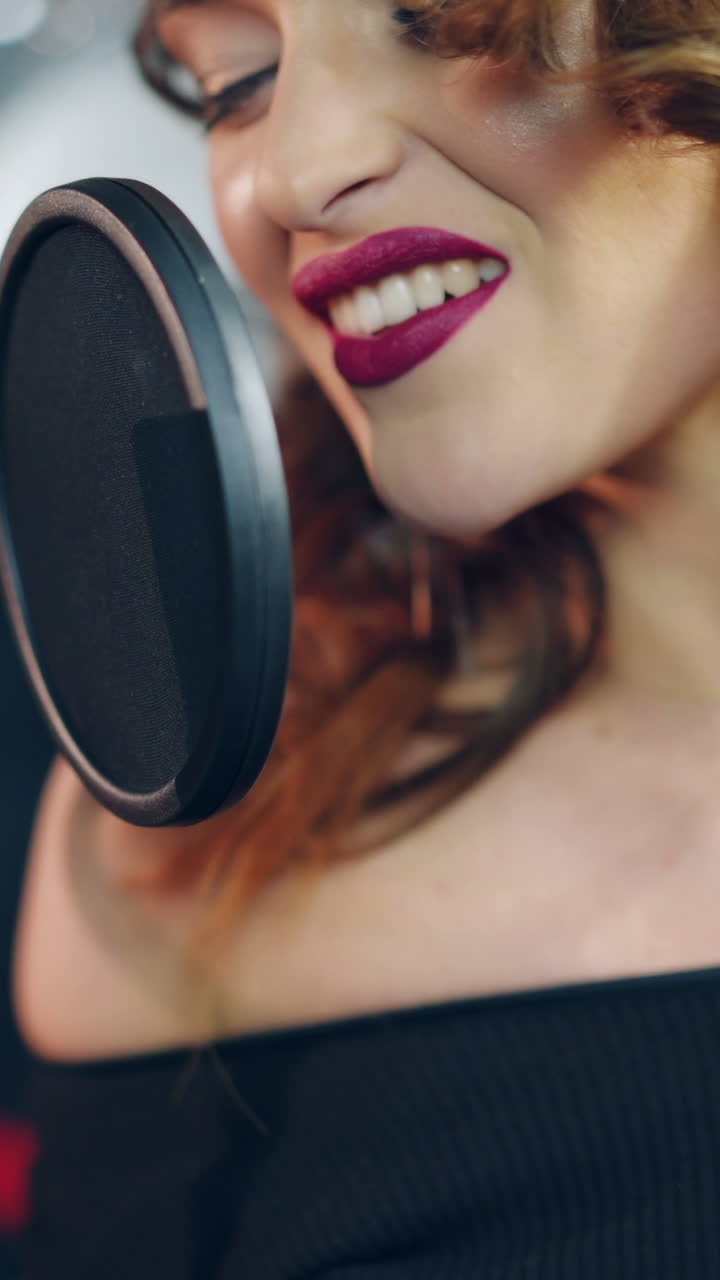a talented woman with bright make-up is singing into a microphone in an audio recording studio. Singer is enjoying singing. Close-up Vertical video