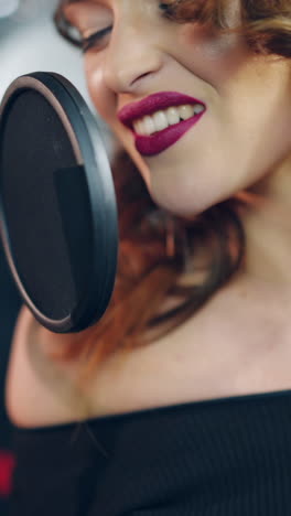 a talented woman with bright make-up is singing into a microphone in an audio recording studio. singer is enjoying singing. close-up vertical video