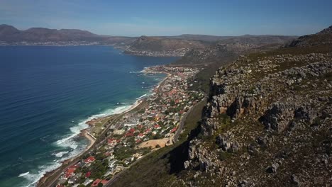 drone descendiendo detrás de las montañas de la mina de plata con el suburbio costero de st james detrás, ciudad del cabo