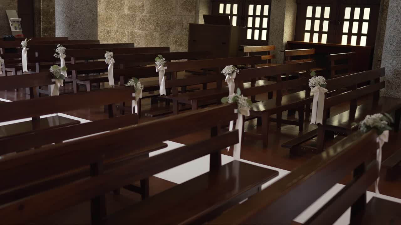 Rows of dark wooden pews decorated with white ribbons and flowers for wedding ceremony