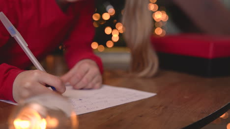 close up view of blonde girl sitting at the table writing on the paper near the christmas tree