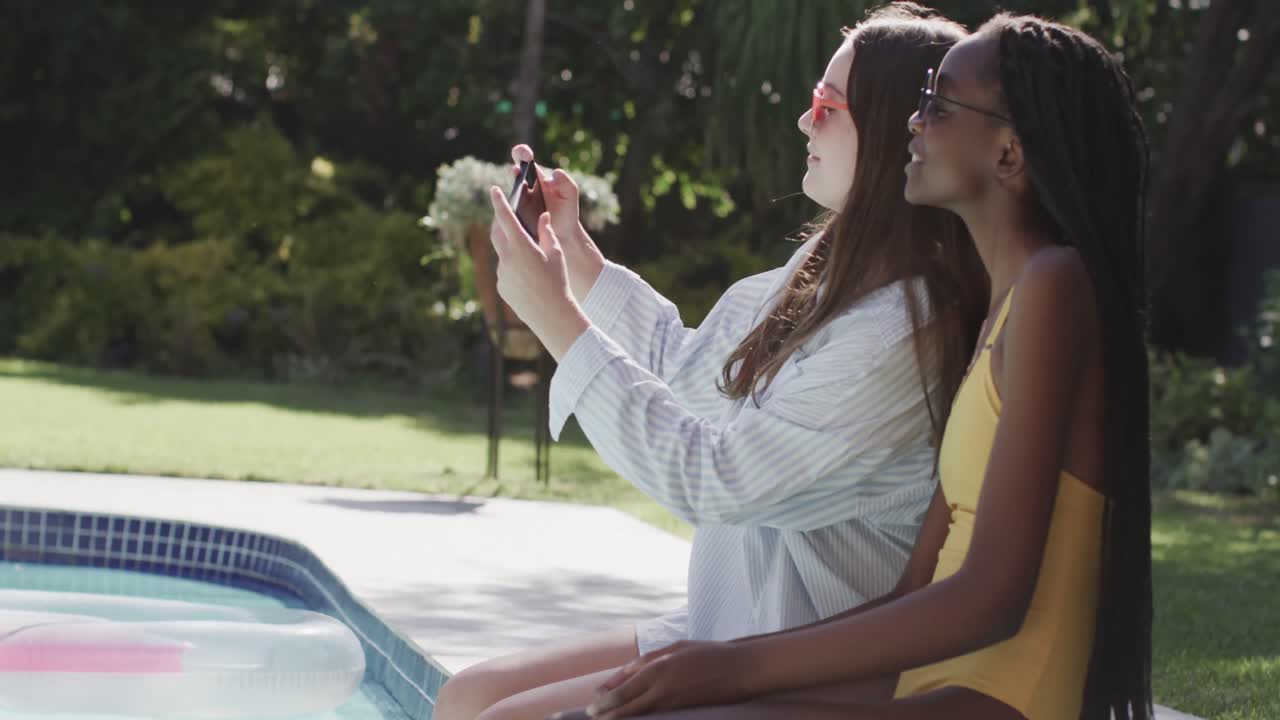 Felici amiche adolescenti di diverse etnie che si scattano un selfie in giardino a bordo piscina al rallentatore.