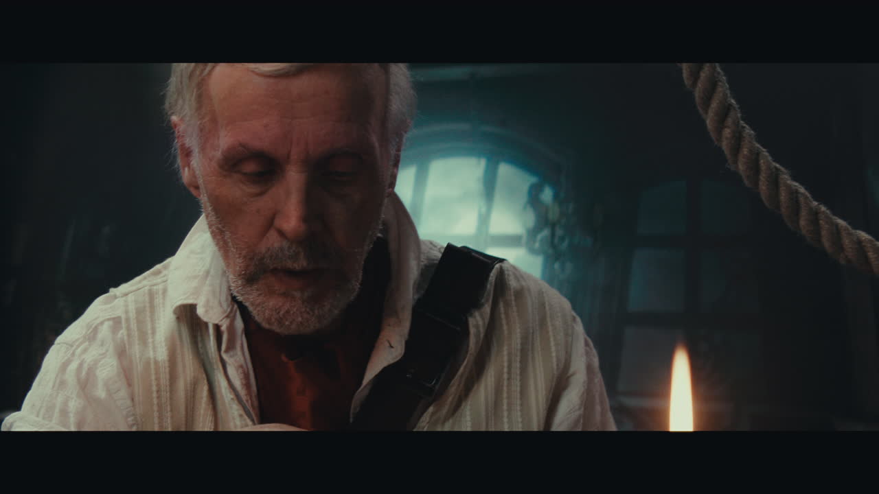 An old pirate eats and drinks inside the sailing ship cabin