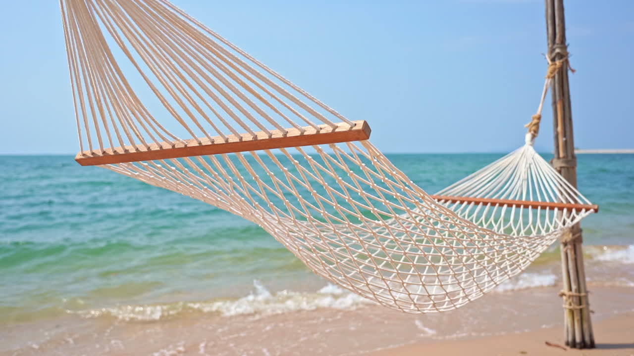 hamaca vacía, hamaca de cuerda balanceándose en la suave brisa de verano que sopla a lo largo de la costa arenosa