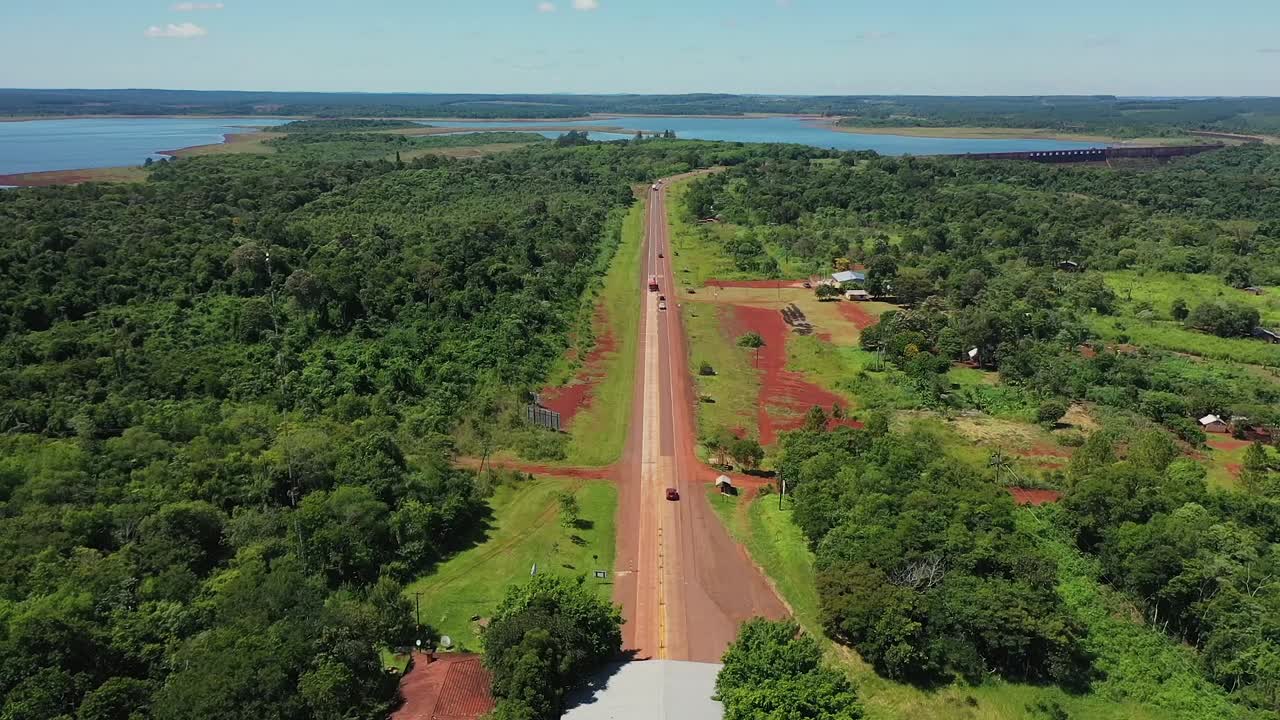 cámara de drones volando hacia atrás revelando una carretera tropical en misiones, argentina donde se puede ver la jungla y un gran lago visto desde arriba