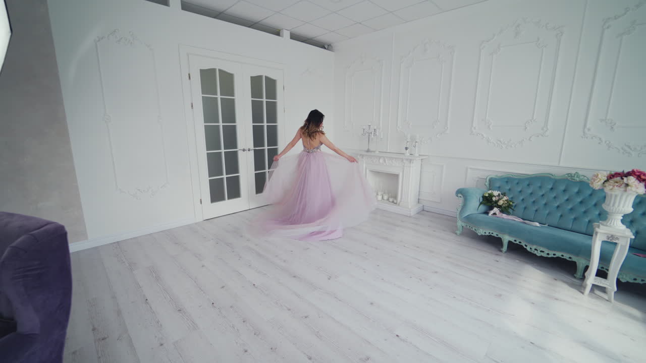 Young model in wedding dress is spinning happily in a spacious room. Romantic bride is posing in a hotel room in her wedding dress.