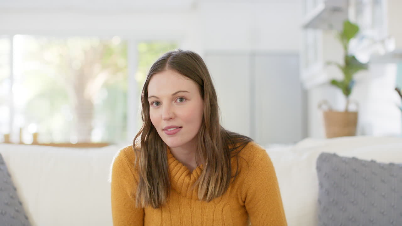Happy caucasian woman sitting on sofa having video call at home, in slow motion