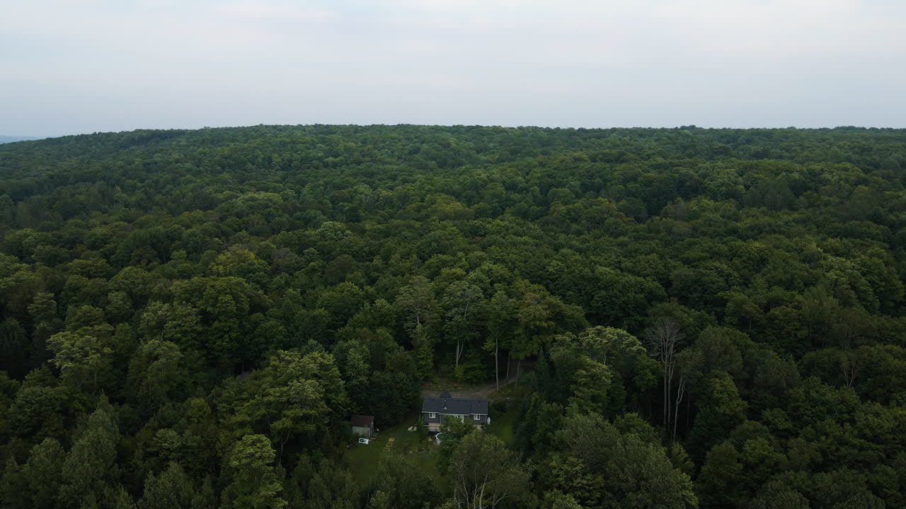 Aerial push in tilted down overview homes surrounded by dense tree forest on cloudy day