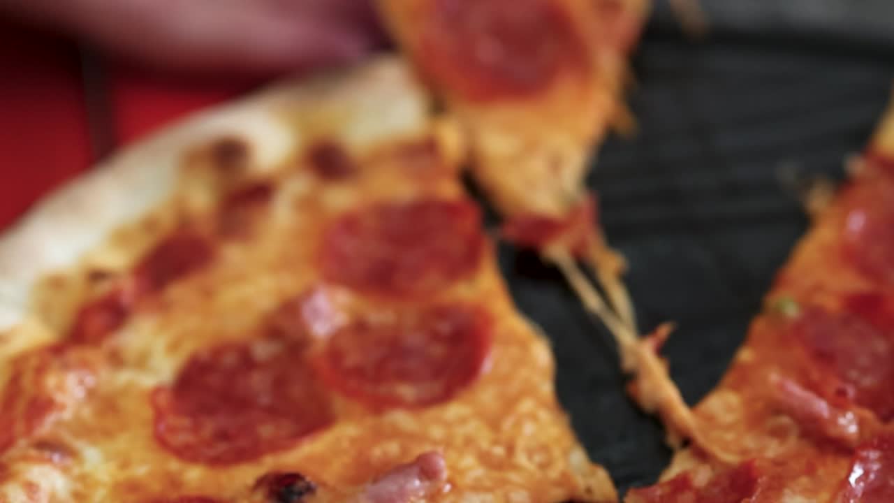 A slice of pepperoni pizza is lifted, revealing gooey cheese against a red background.