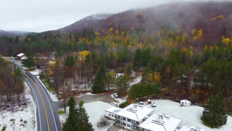 Aerial-View-of-Wet-Backroad-Alongside-Foggy-Green-and-Yellow-Pine-Forest-with-Snow-on-Ground