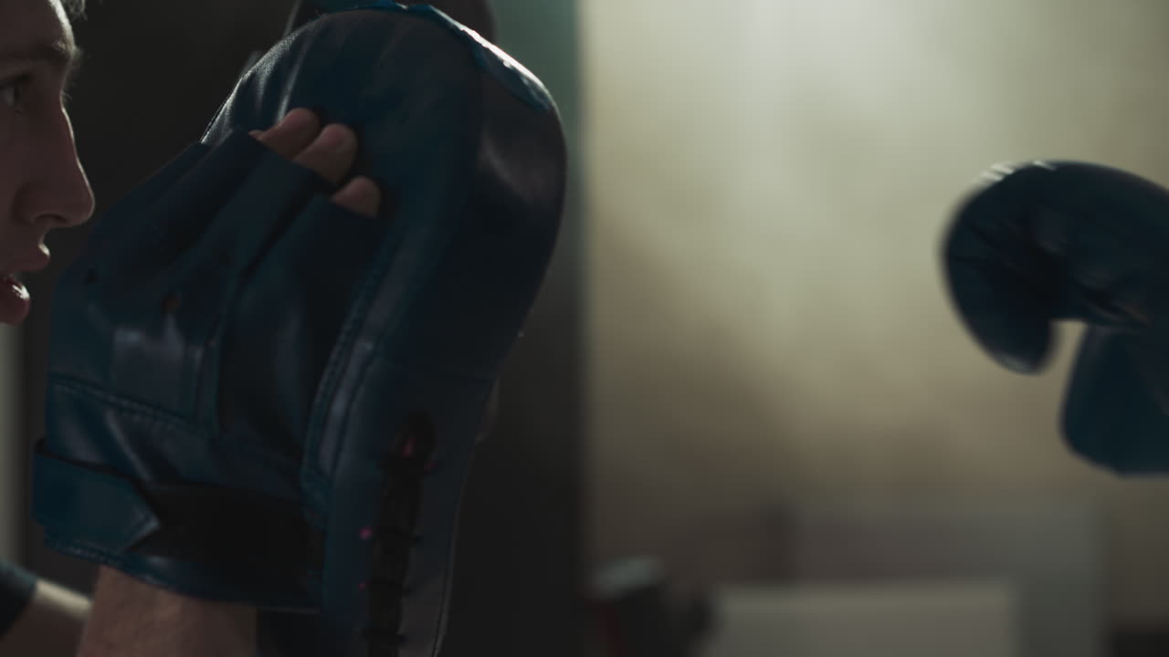 Man holds pads punched by little child in gym closeup. Martial arts trainer works with girl at sparring in sports club slow motion. Combat technique