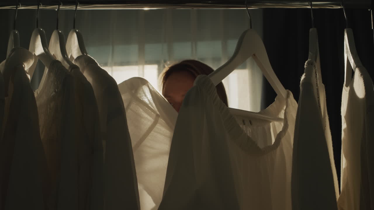 한 여자가 드레싱  ⁇ 에서 옷을 선택합니다.  ⁇ 빛에 실루 ⁇