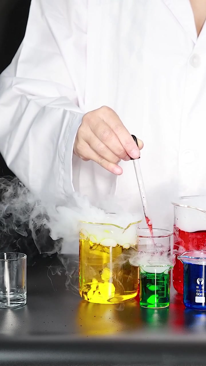 A scientist uses a pipette to mix vibrant liquids in beakers creating thick white smoke.