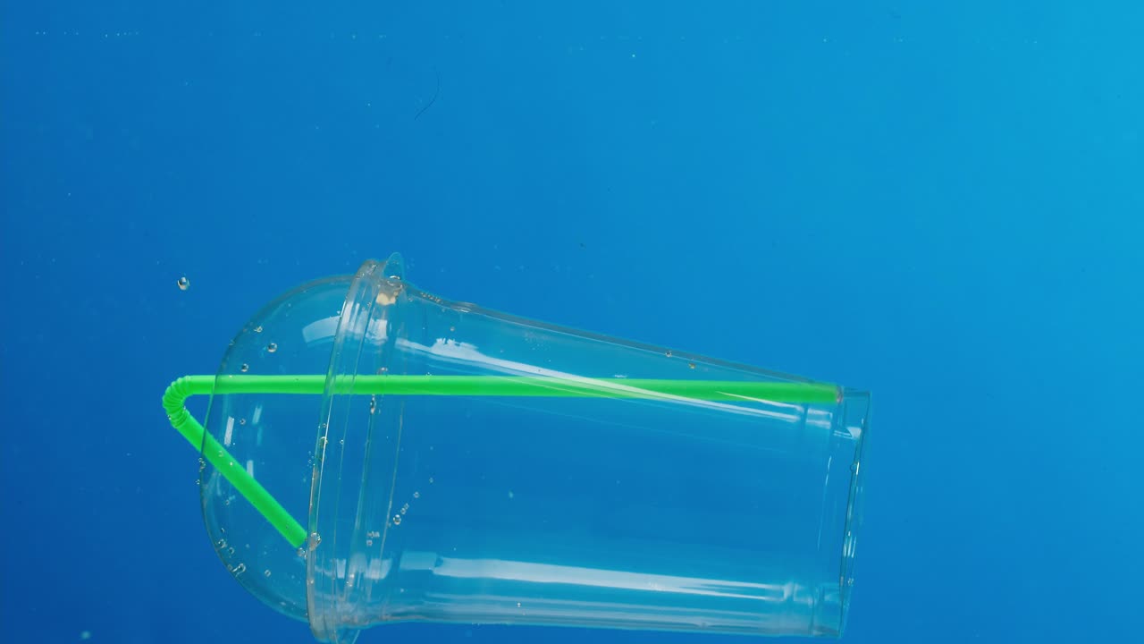 Plastkopp og sugerrør flyter i blått vann