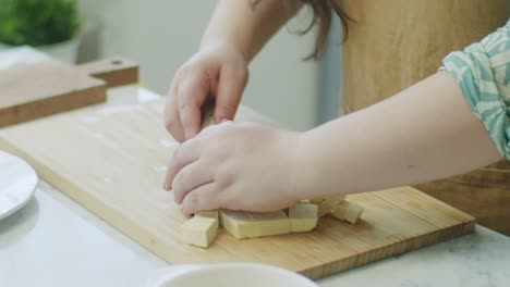 woman shifting cheese cubes from cutting board on plate