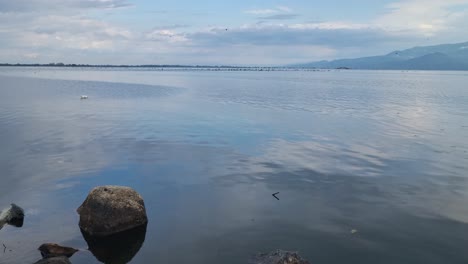 view of kerkini reservoir in northern greece on a cold spring day, with migratory birds visible in the distance, reflecting the tranquil landscape and cloudy sky