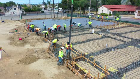 Pull-Back-Aerial-Of-Construction-Workers-At-Construction-Site-With-Giant-Crane-Pouring-Concrete-Foundation-In-Ventura-California