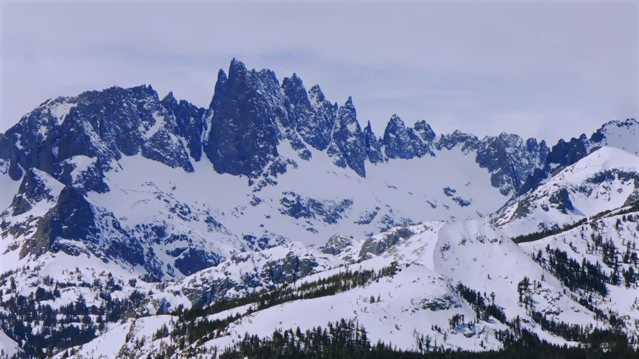 Banner peak Minaret Summit Pass Mammoth Mountains vista Parallax winter aerial drone California group jagged towering snow covered peaks sunny cloudy snow storm Sierra Nevada valley parallax right