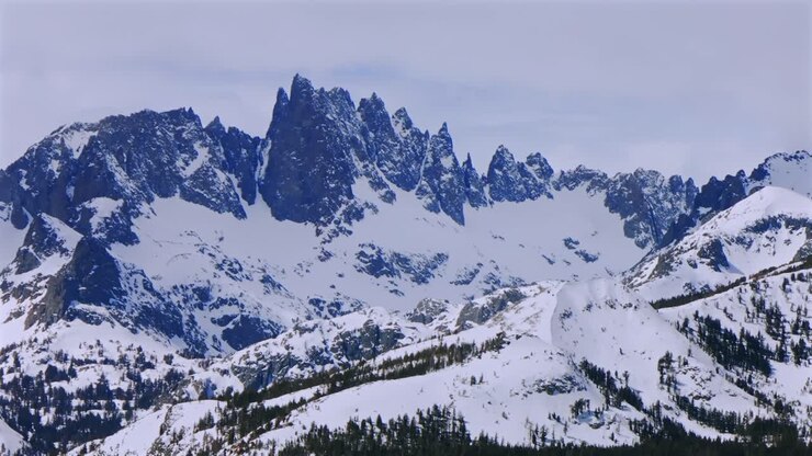 Banner peak Minaret Summit Pass Mammoth Mountains vista Parallax winter aerial drone California group jagged towering snow covered peaks sunny cloudy snow storm Sierra Nevada valley parallax right