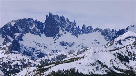 banner peak minaret summit pass mammoth mountains vista parallax winter aerial drone california group jagged towering snow covered peaks sunny cloudy snow storm sierra nevada valley parallax right
