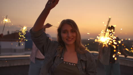 las mujeres en el techo mueven sus brazos y cuerpo hermosamente un baile con sus amigas en una noche de verano con gran luz bengal. es un atardecer de placer antes de la noche. su cabello sopla hermosamente en el viento.