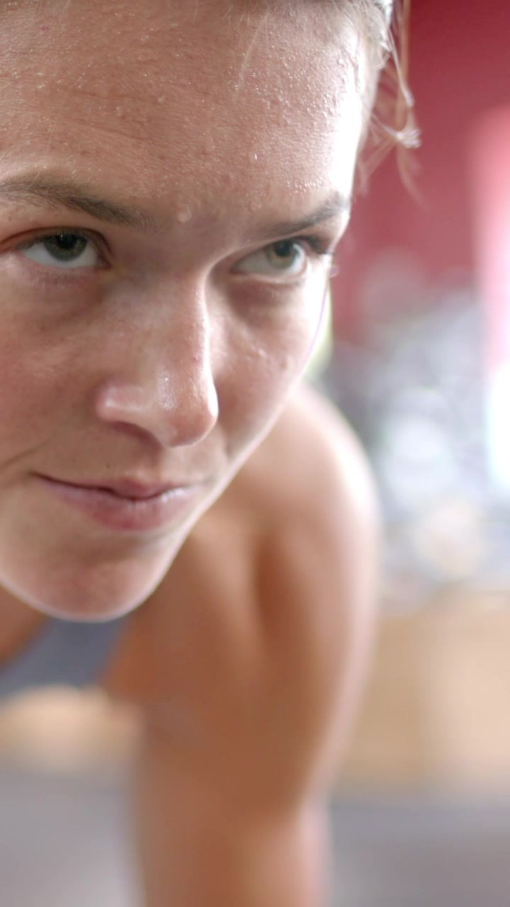 Vertical video: Female athlete gasping, recovering and regaining focus after plank in gym, grey top
