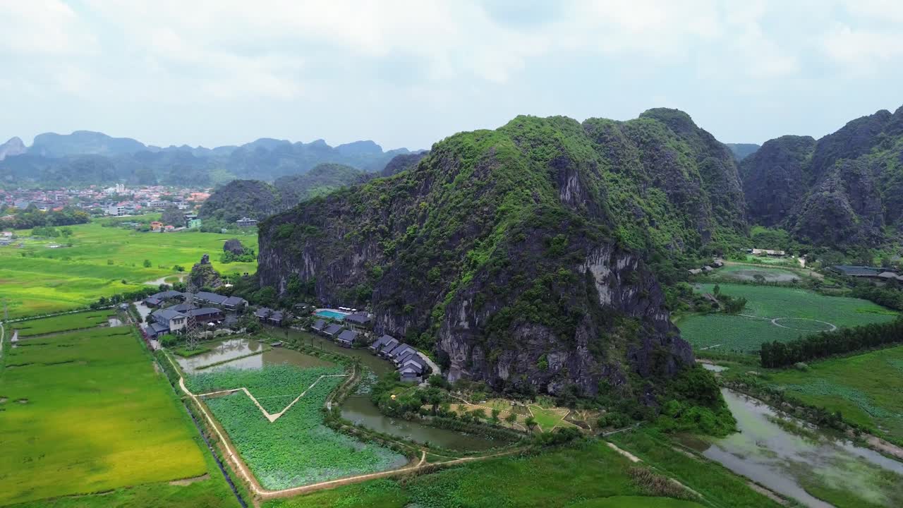 Drone zoom in over green limestone peaks and vivid rice terraces in Ninh Binh under cloudy sky