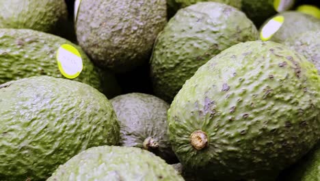 muchos aguacates maduros llenando el marco, creando un fondo texturizado de tonos verdes y marrones, probablemente en un supermercado mexicano, listo para la compra