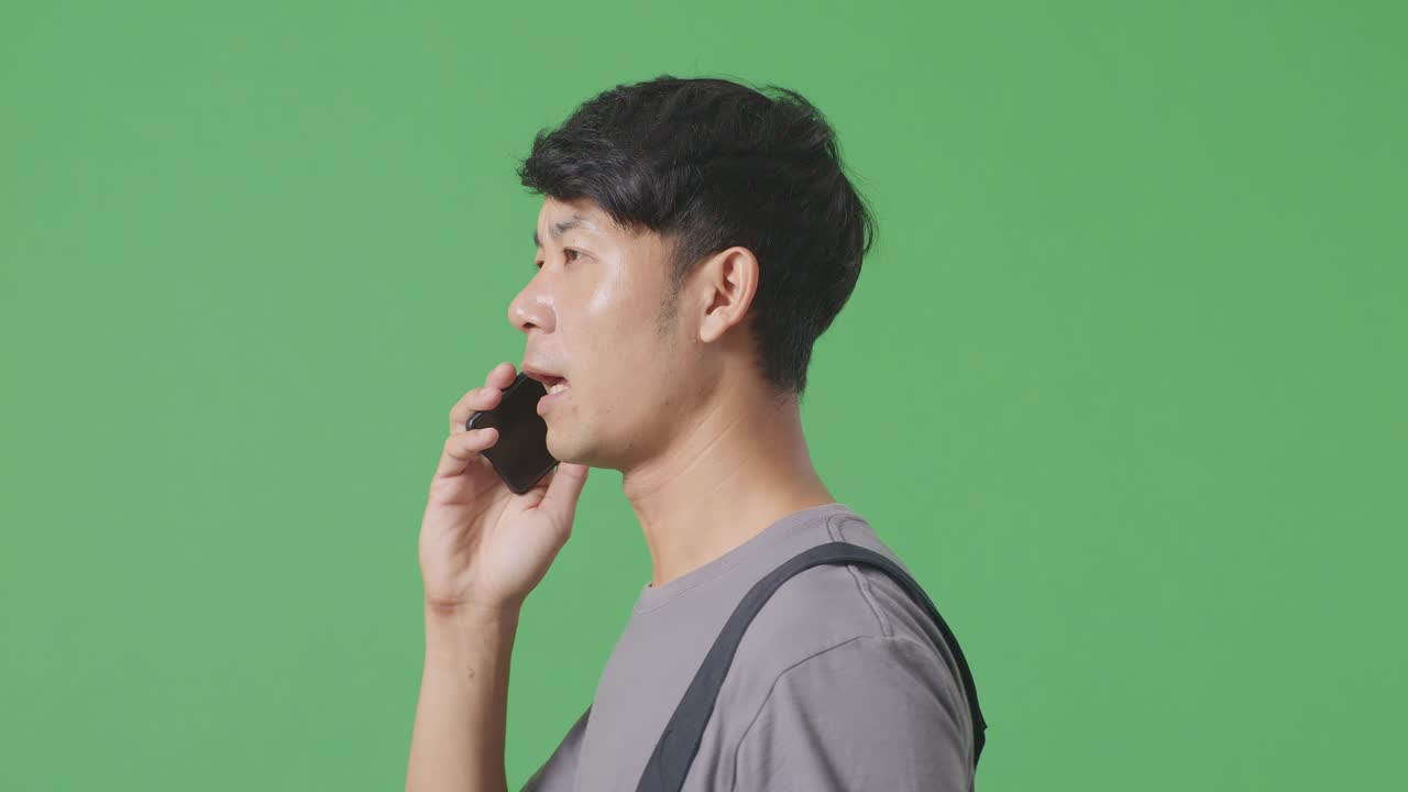 녹색 스크린 배경 스튜디오에서 는 동안 스마트폰으로 이야기하고 주변을 둘러보는 아시아 남성 노동자의 측면 뷰 클로즈업