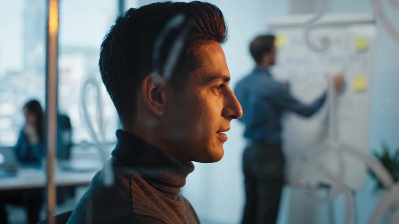 Dyb eftertanke på et samarbejdsorienteret arbejdsområde: En fokuseret person tænker dybt, mens kolleger deltager i en dynamisk brainstorm-aktivitet på en whiteboardtavle.