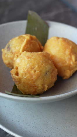 crisp, golden brown papa rellena served on a neutral plate, lit with warm, natural lighting. this vertical video captures a close-up shot ideal for mobile and social media