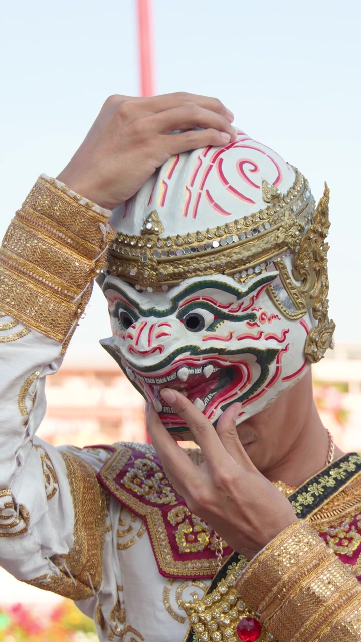 Un ballerino si toglie una maschera bianca di Hanuman, rivelando il suo viso sotto una luce esterna intensa