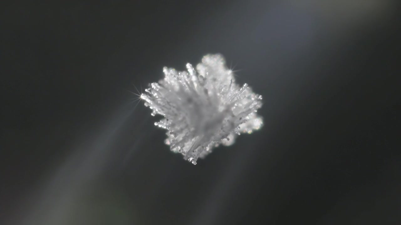 Rotating square crystal under spotlight to reveal facets in studio, with pinpoint glints