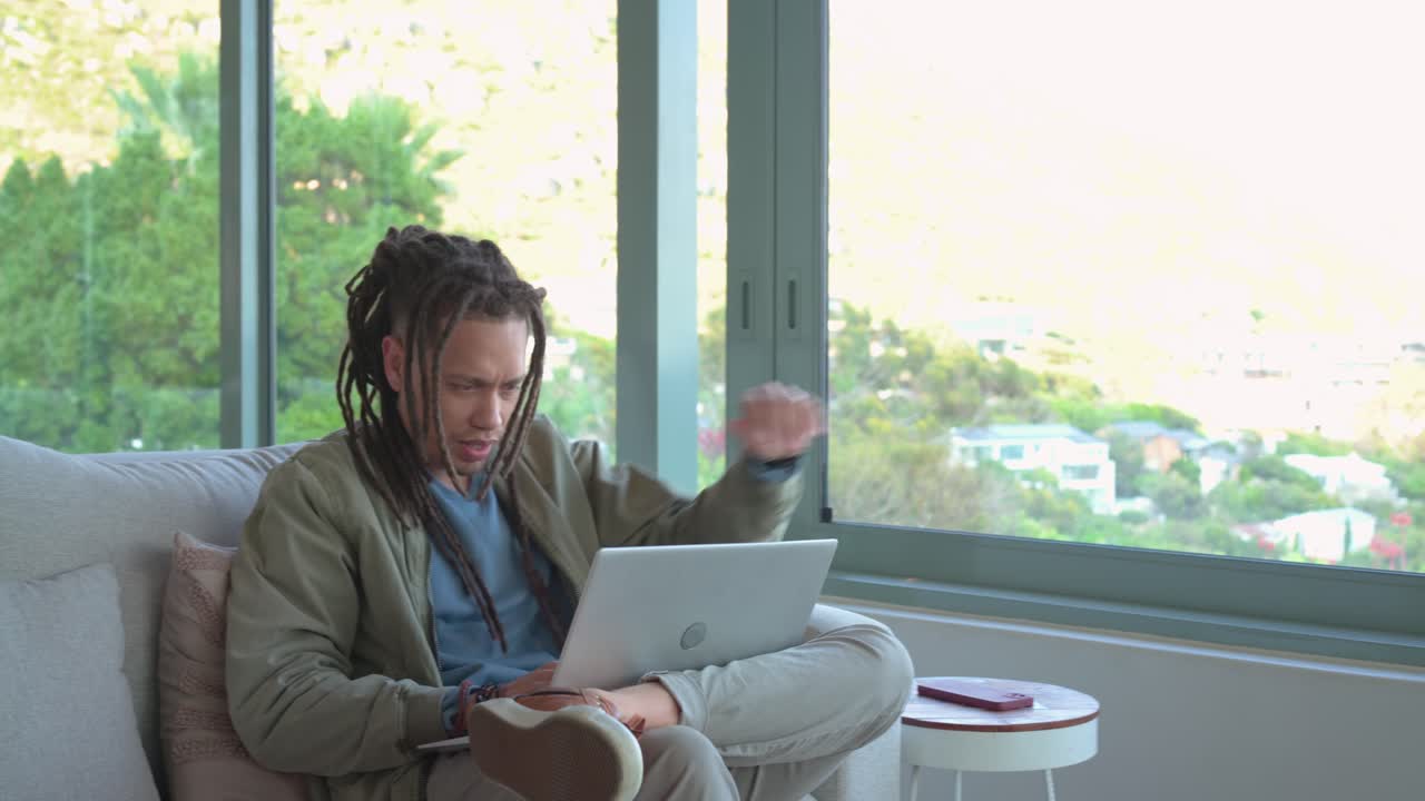 Man wearing jacket holding laptop in glass living room reading screen upset grabbing phone smiling