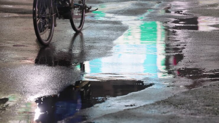 Reflection Of Person On Bicycle Seen At Puddle On Asphalt Road After Raining At Night In Tokyo, Japan