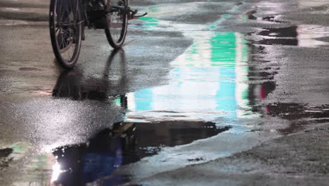 reflection of person on bicycle seen at puddle on asphalt road after raining at night in tokyo, japan