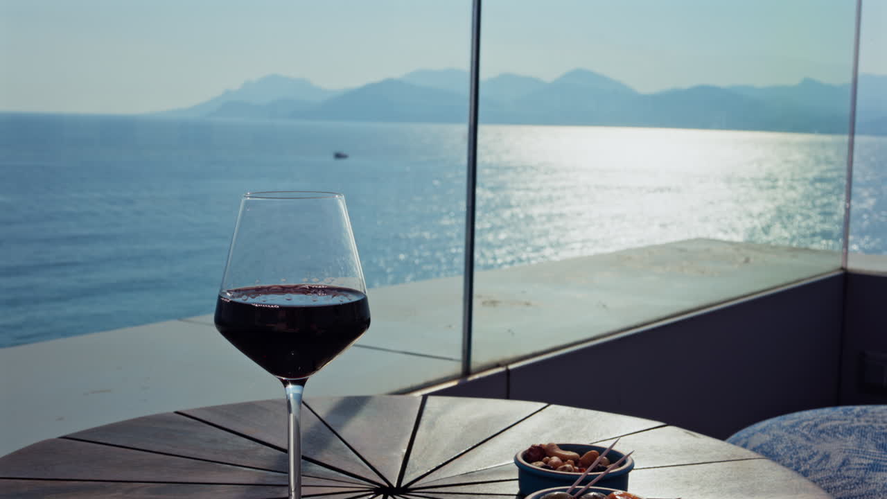 Close up of a glass of red wine and snacks on a table at a terrace with a sea view