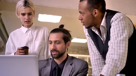 three multy-ethnic workers discuss idea on laptop in office, coworking concept, communication concept