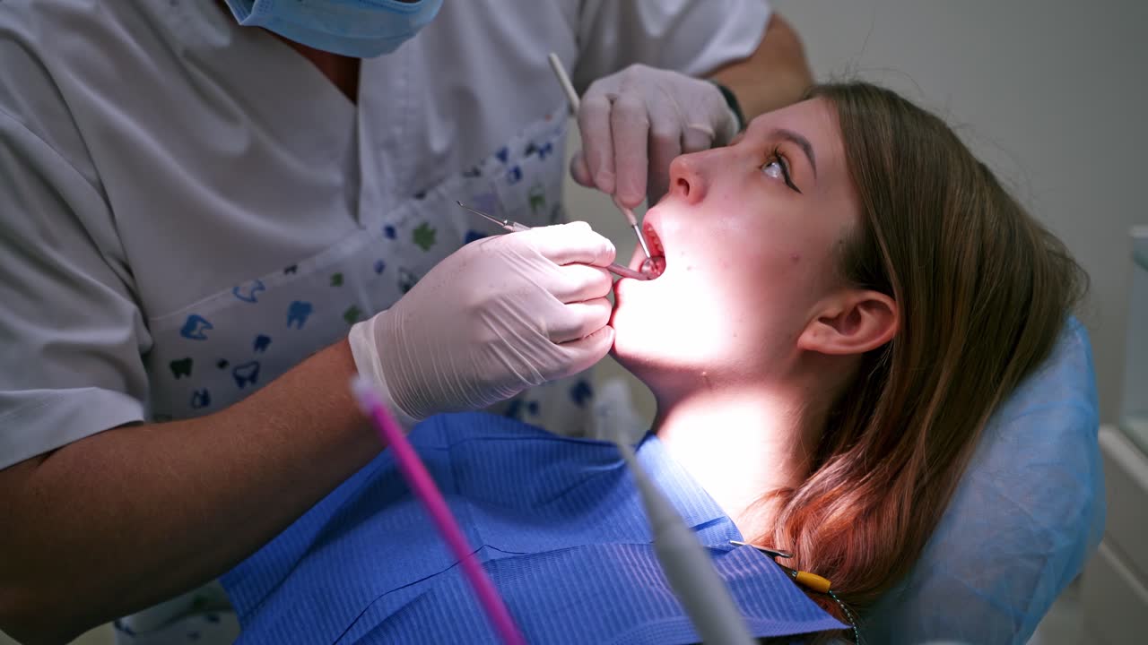 Doctor checks female's teeth. Close-up. Young woman with opened mouth at dentist's office. Stomatologist in sterile gloves treating patient.