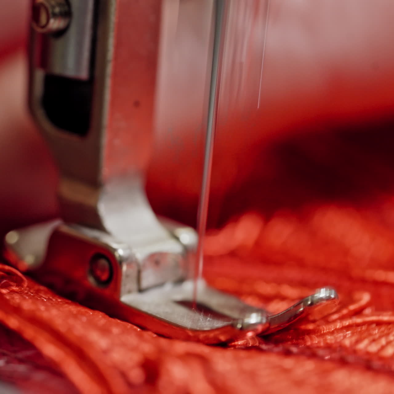 Steel part of sewing machine with a needle working on red cloth. Seamstress woman is sewing on modern machine with red fabric. Close-up