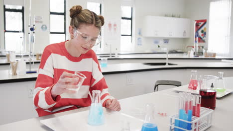 Young girl conducting science experiment in school lab, wearing safety goggles, focused