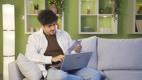 happy young man counting money and looking at laptop.