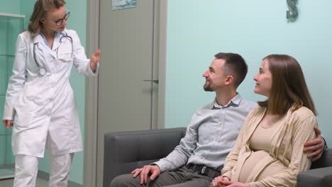 pregnant woman and her husband sitting on sofa waiting for gynecologist in medical consultation