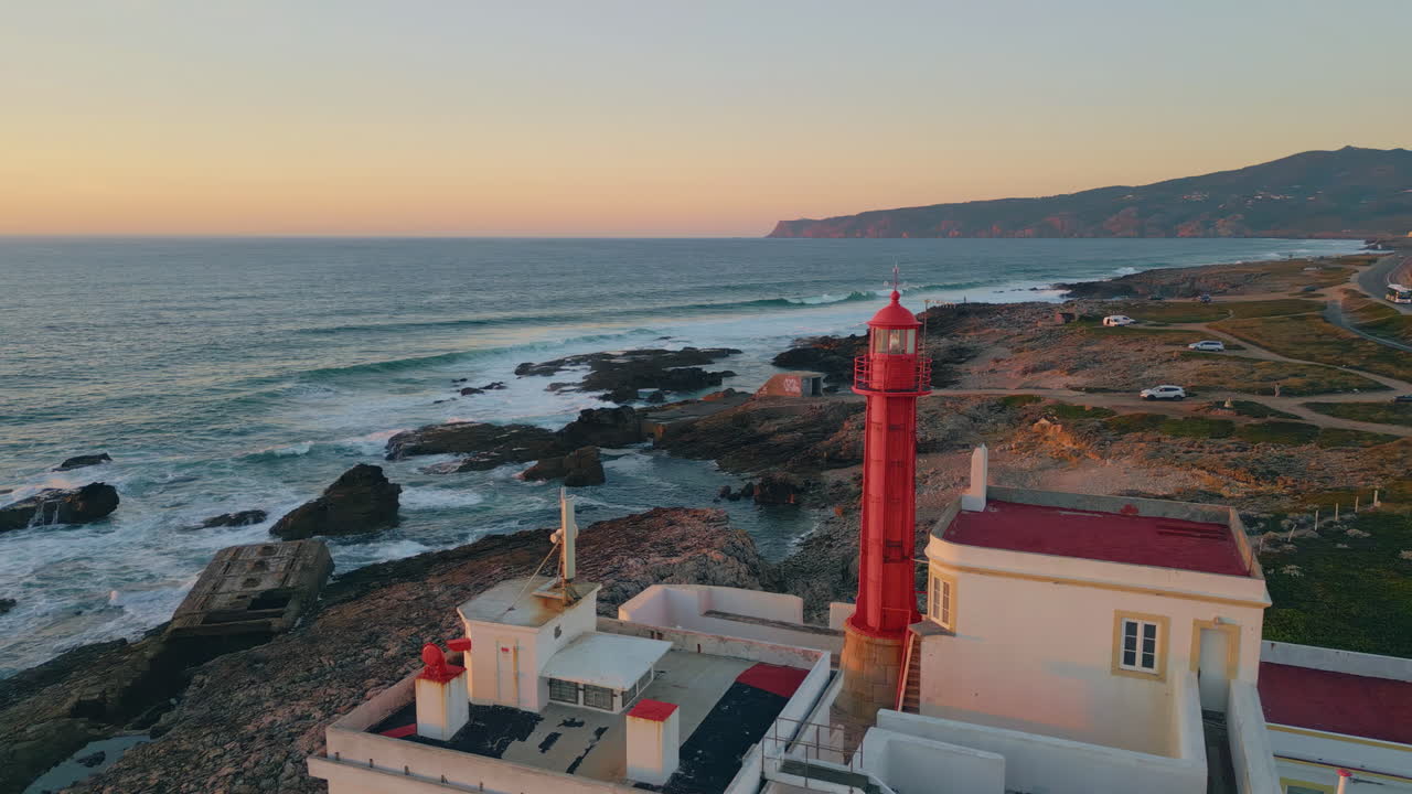 Lighthouse rising evening coast washed by beautiful foamy ocean aerial view.