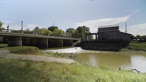 Wide-of-Water-Mill-not-Working-next-to-Bridge-with-Cars-Crossing-over-Water-Falls