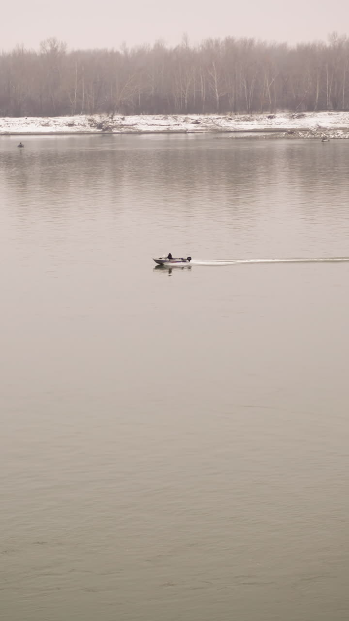 차가운 날씨에 안개가 가득한 분위기와 조용한 물 표면으로 둘러싸인 조용한 장면을 만드는 가운 눈으로 인 해안선에 겨울의 나무를 반영하는 조용한 안개 강에서 평화롭게 항해하는 보트
