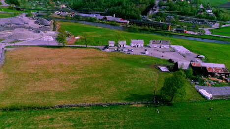 Pueblo-A-Lo-Largo-De-Las-Orillas-Verdes-Del-Río-En-Un-Día-Soleado-De-Verano-Con-Montañas-En-El-Fondo,-Noruega